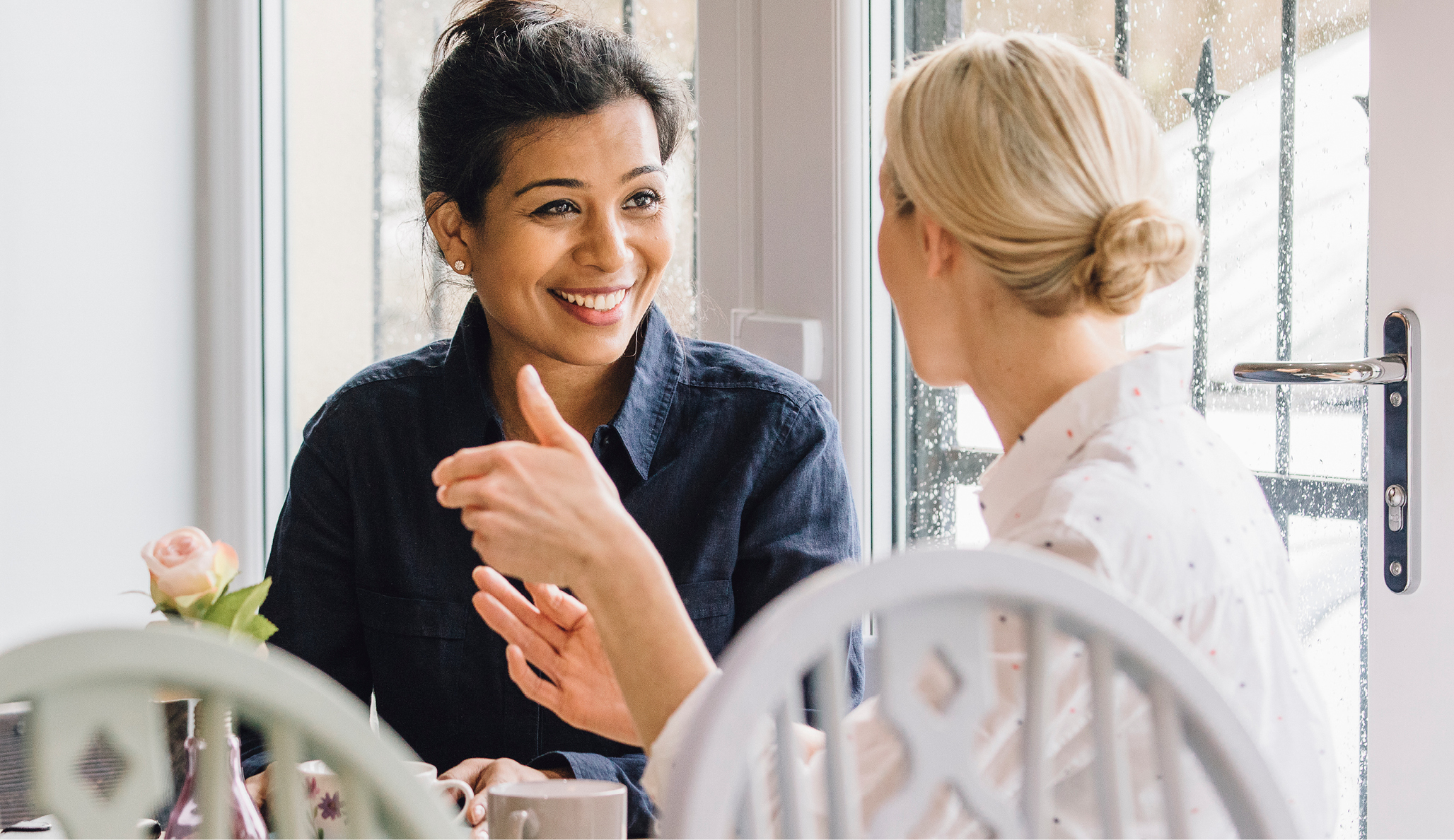 Two women are sitting together at a table, talking and smiling. 