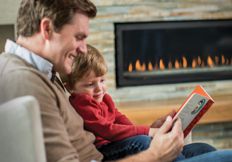 A man and a child read together in front of a propane fireplace.