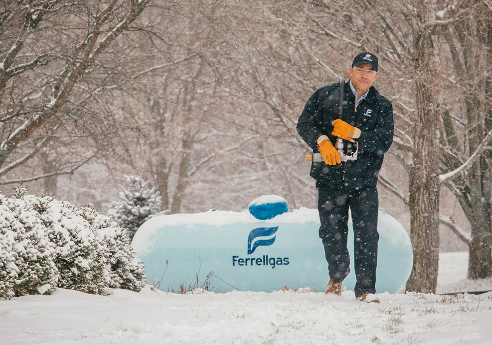 Ferrellgas employee walking near residential propane tank in winter.