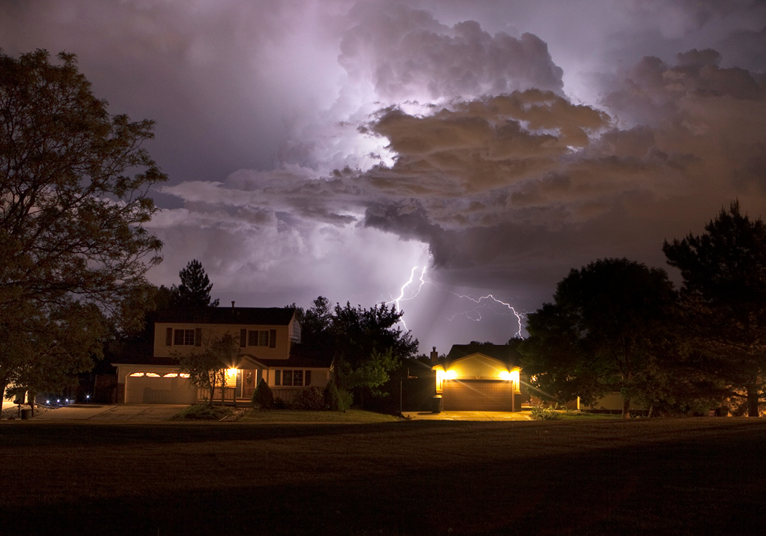 Photo of a house at night during a lightning storm.